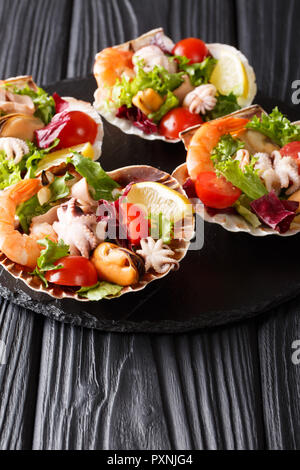 Ristorante gourmet a base di pesce insalata di gamberetti, polipetti, cozze, calamari e capesante in conchiglie di mare vicino sul piano verticale. Foto Stock
