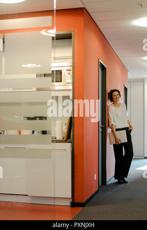 Ridendo imprenditrice in piedi nel corridoio di ufficio, tenendo laptop Foto Stock