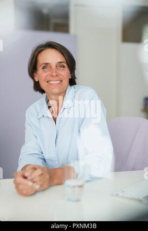 Ritratto di sorridente imprenditrice maturo seduto alla scrivania Foto Stock