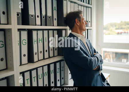 Imprenditore in archivio aziendale, appoggiata contro uno scaffale con i file Foto Stock