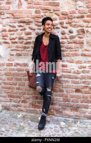 Ritratto di sorridente giovane donna appoggiata contro un muro di mattoni Foto Stock