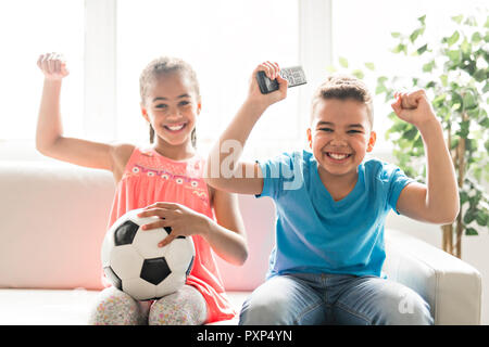 Fratello e Sorella con pallone da calcio ascolto gioco di piede sulla tv Foto Stock