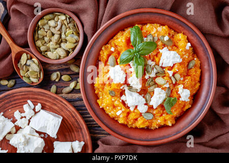 Butternut cremosa di zucca e feta Mash con riso cosparso con i semi di zucca e decorate con foglie di basilico fresco su una piastra di terracotta con ingre Foto Stock