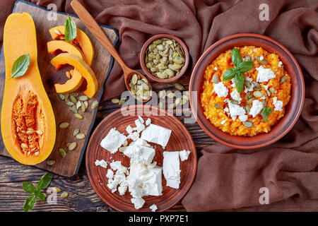 Butternut cremosa di zucca e feta Mash con riso cosparso con i semi di zucca, basilico foglie su un piatto di terracotta con ingredienti su una tavola di legno la ruggine Foto Stock