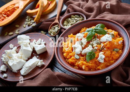 Close-up di butternut cremosa di zucca e feta Mash con riso cosparso con i semi di zucca e decorate con foglie di basilico fresco su un coccio plat Foto Stock