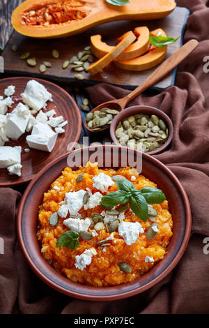 La zucca mash con riso e formaggio feta cosparso con i semi di zucca e decorate con foglie di basilico fresco su una piastra di terracotta con ingredi Foto Stock