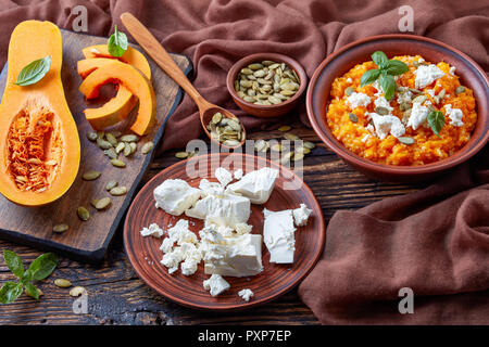 Close-up di crema di zucca butternut e purea di feta con riso cosparso con i semi di zucca e decorate con foglie di basilico fresco su un coccio pla Foto Stock