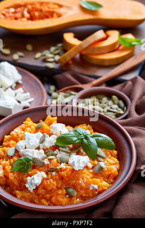 Crema di zucca butternut e purea di feta con riso e semi di zucca e di foglie di basilico fresco su una piastra di terracotta con ingredienti su un rustico in legno ta Foto Stock