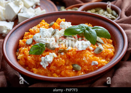 Crema di zucca butternut e purea di riso con formaggio feta, semi di zucca e di foglie di basilico fresco in un vaso di argilla con ingredienti su un rustico in legno tabl Foto Stock