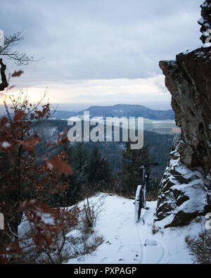 Il sentiero coperto di neve e una mountain bike. nella parte anteriore del paesaggio invernale su una montagna sotto una roccia. focus in mtb. Foresta Nera, Germania Foto Stock