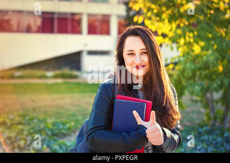 Donna giovane studente a piedi nel campus universitario mostra Thumbs up gesto. Foto Stock