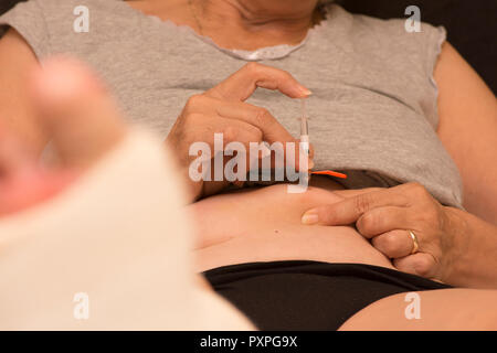 Donna di iniettare il suo pancino con Fragmin, un anti-cagulent per prevenire la formazione di coaguli di sangue dopo un intervento sul piede che è ora in gesso. Foto Stock