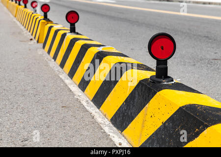 I blocchi di calcestruzzo con cautela striped pattern, recinzione stradale con riflettori rossi Foto Stock