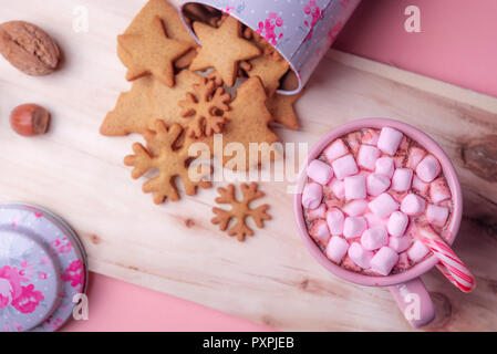 I dolci di Natale il contesto con una tazza di cioccolata calda con mini rosa marshmallows, una scatola rovesciata con pan di zenzero i cookie su un tagliere di legno. Foto Stock