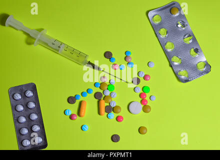 Un assortimento di medicinali, pillole in confezioni, capsule, multi-colore di vitamine e una siringa con un ago su un giallo-sfondo verde Foto Stock