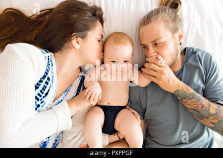 Ritratto di felice giovani genitori con il bambino nel letto di casa Foto Stock