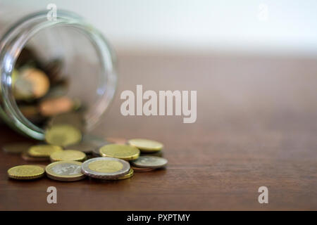 La fuoriuscita di monete da un vaso di vetro su di un tavolo di legno Foto Stock