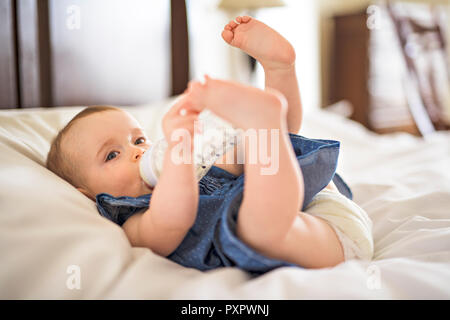 Graziosa bambina beve acqua dalla bottiglia giacente sul letto Foto Stock