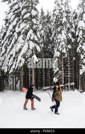L'Italia, Modena, Cimone, giovane con sci e snowboard e passeggiate nella foresta di inverno Foto Stock