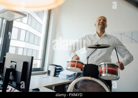 Imprenditore facendo rumore con tamburi nel suo ufficio Foto Stock