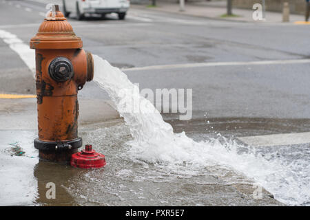 Orange idrante di fuoco aperto e acqua zampillante sul marciapiede e la strada Foto Stock