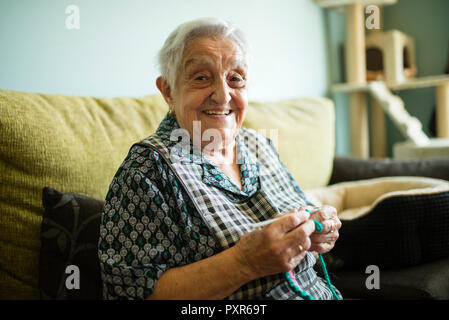 Ritratto di sorridente donna senior a crochet sul lettino a casa Foto Stock