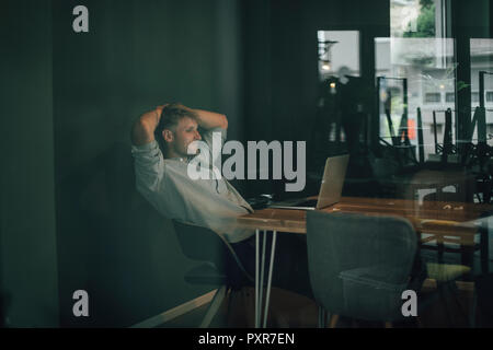 Uomo seduto in ufficio, lavora fino a tardi nella sua azienda start-up Foto Stock