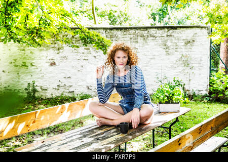 Ritratto di giovane sorridente donna seduta sul tavolo della birra in giardino Foto Stock