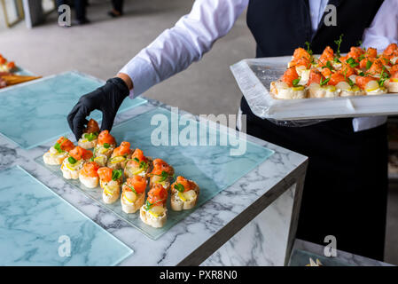 Mani in guanti con il cibo sulla tavola per banchetti Foto Stock