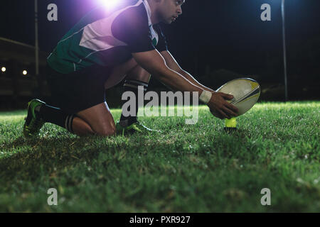 giocatore di rugby che mette la palla sul tee per il tiro di rigore durante la partita. giocatore di rugby che fa un tiro di rigore sotto le luci nell'arena sportiva. Foto Stock