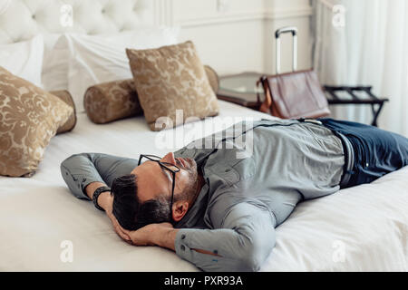 Ritratto di stanchi imprenditore caucasico dormire su un letto in una camera d'albergo. Imprenditore maturo rilassante sul letto dopo il viaggio. Foto Stock