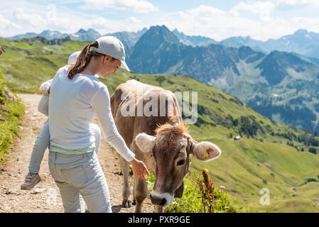 In Germania, in Baviera, Oberstdorf, madre e figlia piccola riunione una mucca durante una escursione in montagna Foto Stock