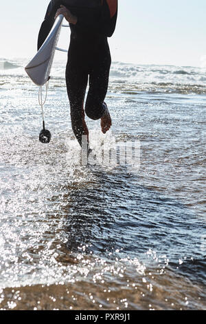 Il Portogallo, Algarve, uomo in esecuzione in acqua con la tavola da surf Foto Stock