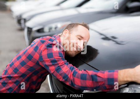 Un Felice giovane uomo abbraccia il suo auto al di fuori del garage negozio Foto Stock