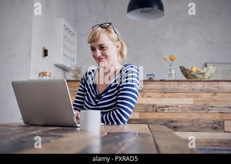 Ritratto di donna sorridente seduta a tavola con laptop Foto Stock