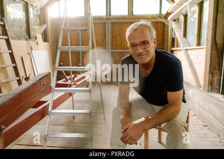 Ritratto di un fiducioso uomo maturo seduto nel suo laboratorio Foto Stock