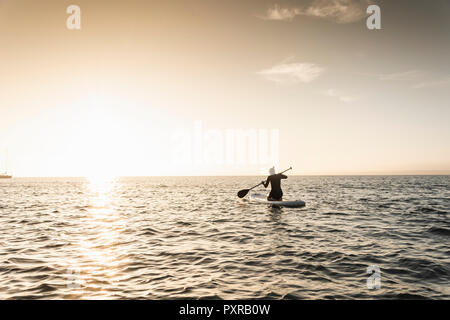 Giovane donna stand up paddle surf al tramonto Foto Stock