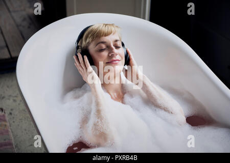 Donna bionda tenendo bagno di bolle in un loft listenung musica con le cuffie Foto Stock