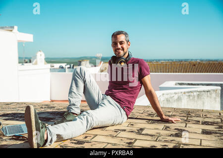 Uomo sorridente seduto sul tetto, godendo di estate Foto Stock