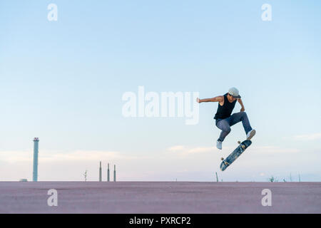 Giovane uomo facendo uno skateboard trick su una corsia al crepuscolo Foto Stock