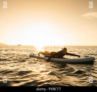 Giovane donna sdraiata su paddleboard al tramonto Foto Stock