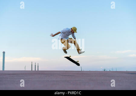 Giovane uomo facendo uno skateboard trick su una corsia al crepuscolo Foto Stock