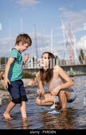 Germania, Friedrichshafen, Lago di Costanza, felice madre e figlio con barca giocattolo sul lungolago Foto Stock