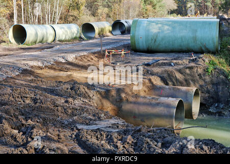 Grandi tubi di cucitore giacciono sulla sabbia e sporcizia in una foresta di autunno sito in costruzione. Soleggiata giornata di ottobre outoor scatti industriale Foto Stock