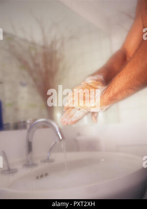 Uomo di lavaggio e di lavaggio delle mani con vigore contro un dolce sottofondo nella stanza da bagno Foto Stock