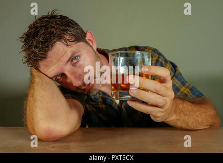 Isolato Ritratto di giovane confuso premuto uomo alcolica avente un drink guardando il bicchiere di whiskey cadere nella tentazione di abuso di alcool in dipendenza s Foto Stock