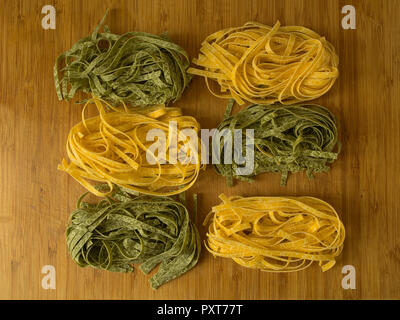 Nidi di non cotti giallo e verde chiamato pasta tagliatelle o fetuccine su un tavolo di legno, Foto Stock