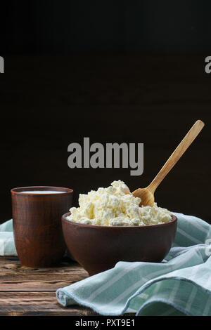 Per la ricotta con il cucchiaio di legno in esso e il latte in clayware sul tavolo di legno Foto Stock