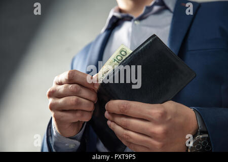 Uomo elegante in tuta tira fuori il suo denaro dal portafoglio. Concezione della gestione del denaro. Foto Stock