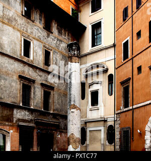 Antico romano colonna dall'Odeon di Domiziano nel mezzo di una piazza romana. La parete del palazzo a sinistra è dipinta con figure del Rinascimento. Foto Stock